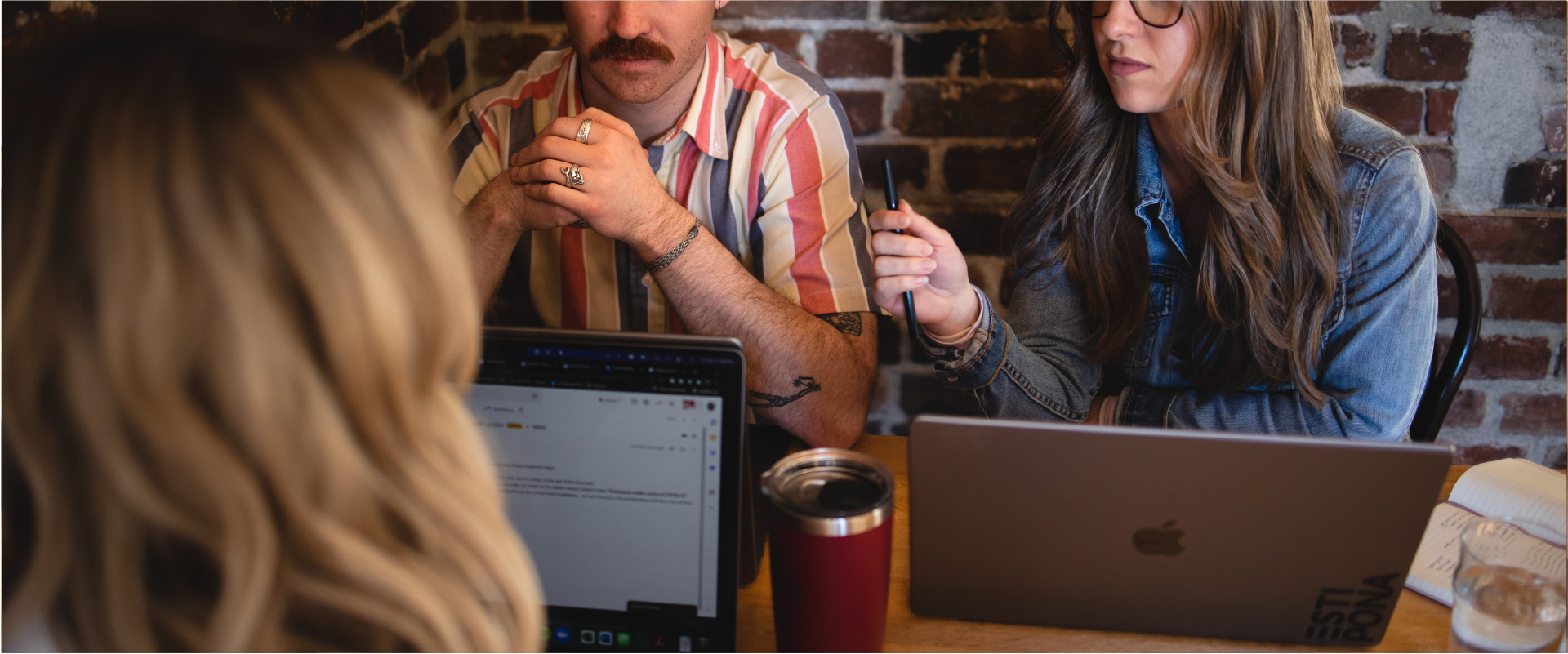 Three people discussing around Apple laptops at a table