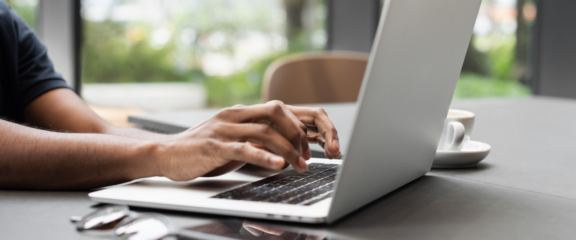 Someone typing on a laptop. Image of just the arms and laptop on a table.